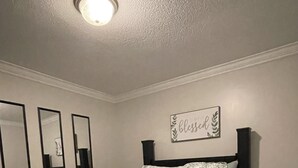 A bedroom with a bed, a nightstand, a wall-mounted mirror, and a ceiling light.