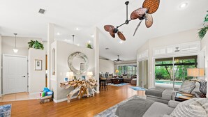 Un salon spacieux doté de planchers en bois franc, d’un canapé gris et d’un ventilateur de plafond.