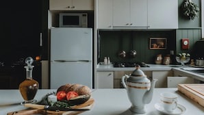 A modern kitchen with a microwave, refrigerator, and a wooden cutting board with fresh vegetables. - Boutique central apartment|private balcony|parking (Docklands)