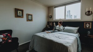A bedroom with a bed, a chair, and a window with a city view. - Boutique central apartment|private balcony|parking (Docklands)