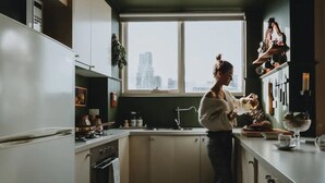 A kitchen with a window view of a cityscape, a sink, cabinets, and a countertop with various items. - Boutique central apartment|private balcony|parking (Docklands)