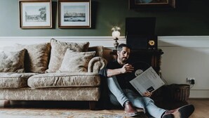 A man sitting on the floor reading a magazine in a room with a sofa, a lamp, and framed pictures on the wall. - Boutique central apartment|private balcony|parking (Docklands)