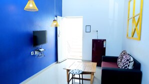 Una habitación con pared azul, una mesa de madera con una silla, un sofá negro, un televisor y una lámpara.
