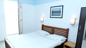 Una cama bien hecha en una habitación con cabecera de madera, un taburete pequeño de madera y dos luces fijadas a la pared.