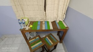 Une petite table en bois recouverte d’une nappe à rayures, un panier rempli de bouteilles d’eau et un petit sac posé sur le sol.
