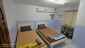 Une petite chambre propre, avec deux lits simples, un bureau et une chaise.