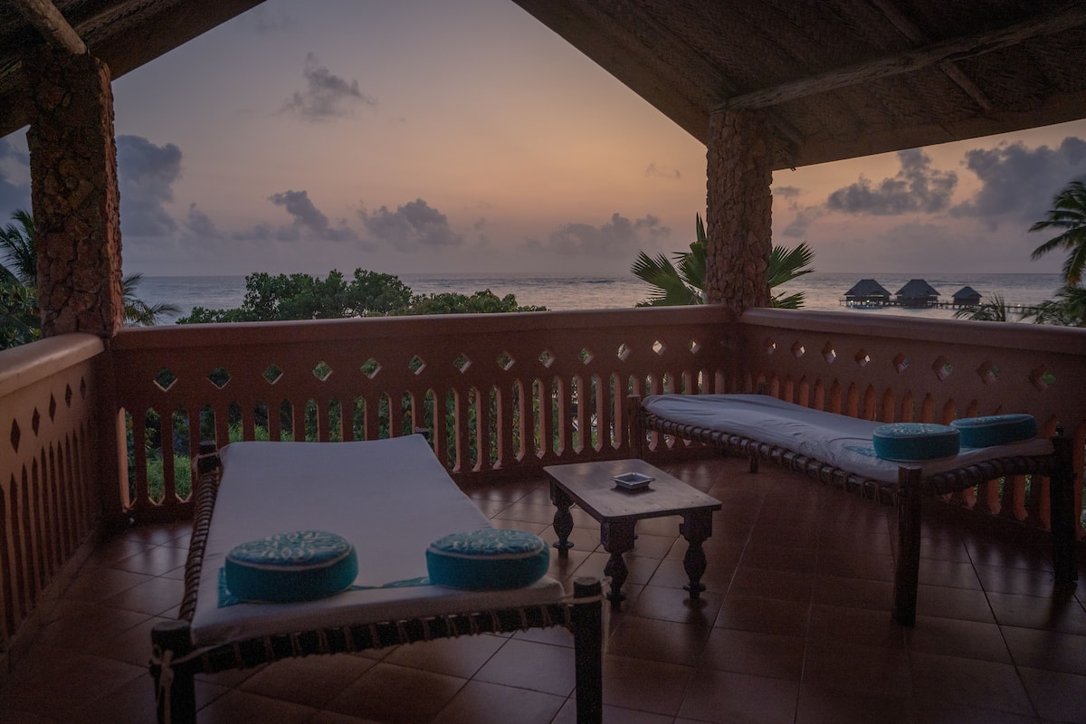 A covered outdoor seating area with a view of the ocean at sunset.