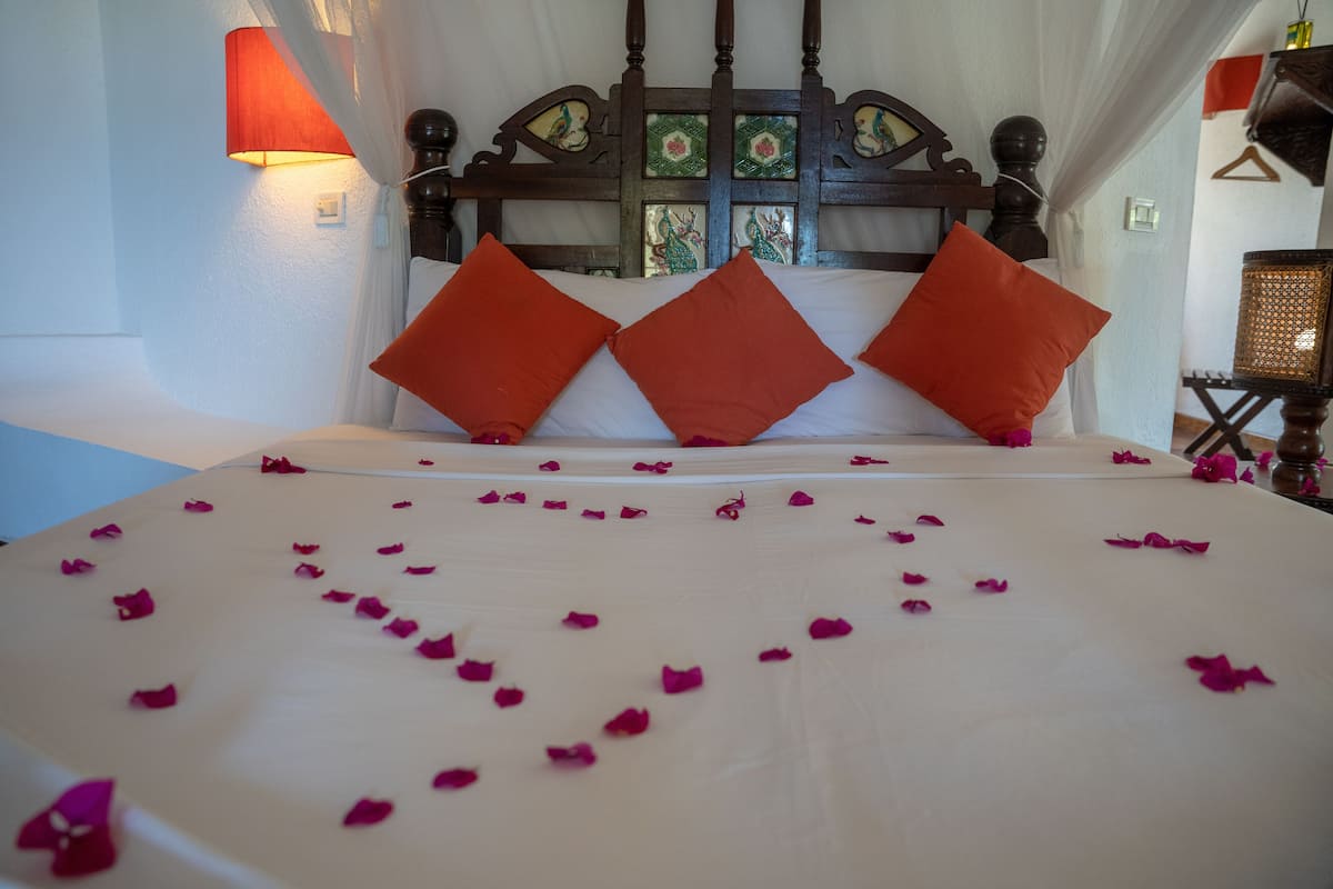 A bed with rose petals, two orange pillows, and a wooden headboard with decorative panels.