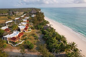 Vista aérea de un resort con villas frente a la playa, una playa de arena y palmeras.