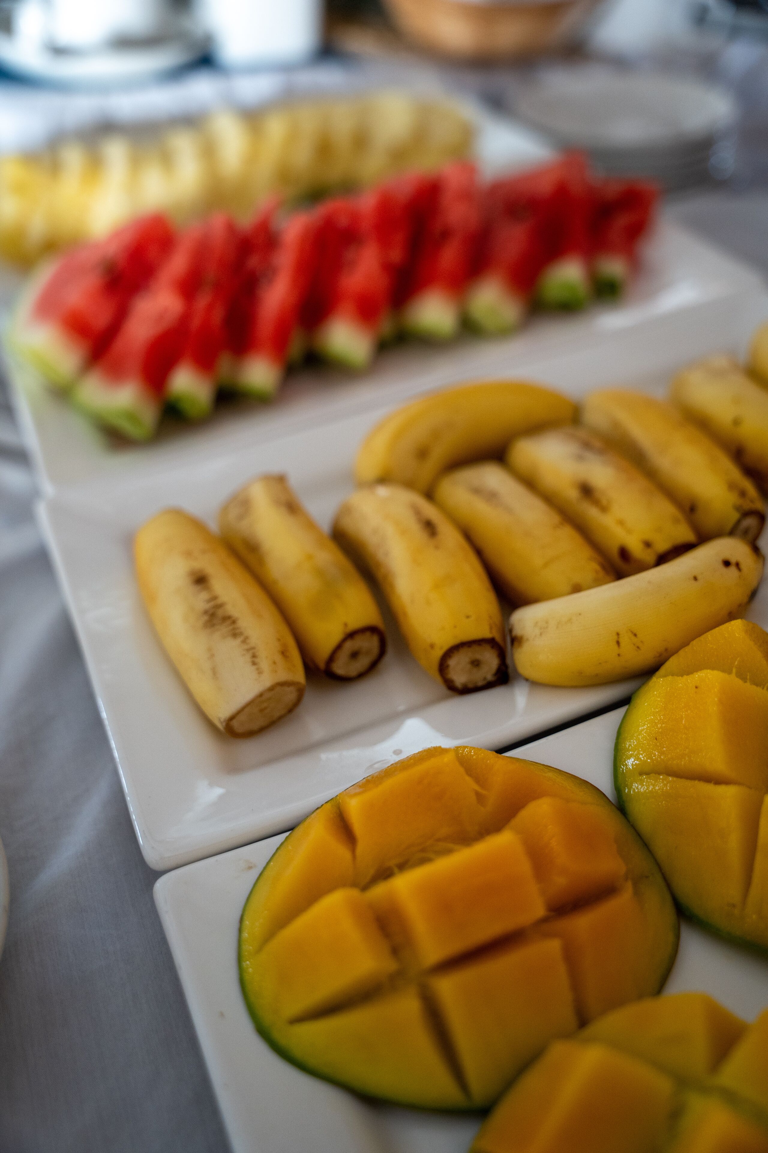 A white rectangular plate with sliced watermelon, bananas, and mango pieces.