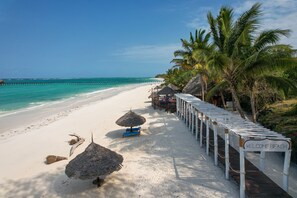 A beach with a wooden walkway, palm trees, and a pier in the background. - SULTAN PALACE (Dongwe)