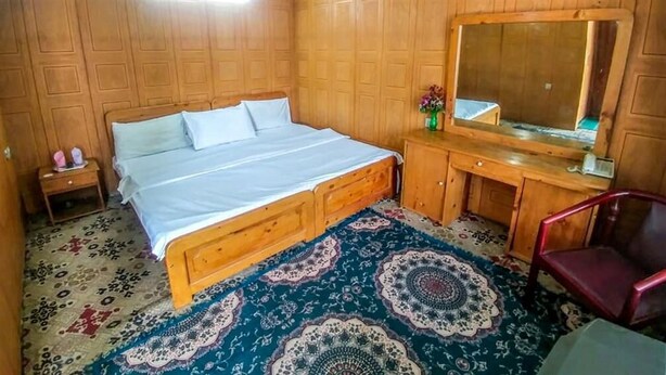 Une chambre à coucher avec un lit en bois, une table de chevet, une commode, un miroir et un tapis à motifs.