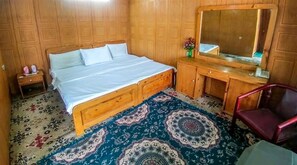 A bedroom with a wooden bed, a nightstand, a dresser, a mirror, and a patterned rug. - DEWAN E KHAS Hotel Skardu (Skardu)