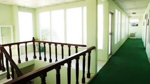 Un couloir d’hôtel avec un tapis vert, une rambarde en bois et de grandes fenêtres.