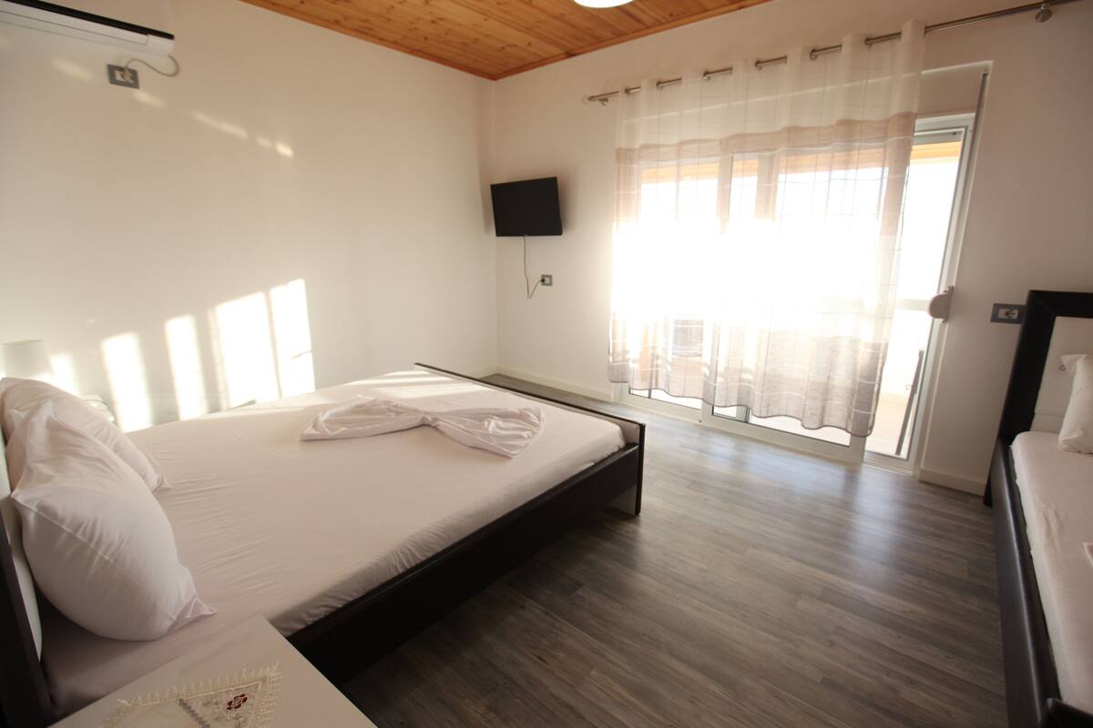 Un dormitorio con una cama, un televisor en la pared y una ventana con cortinas.