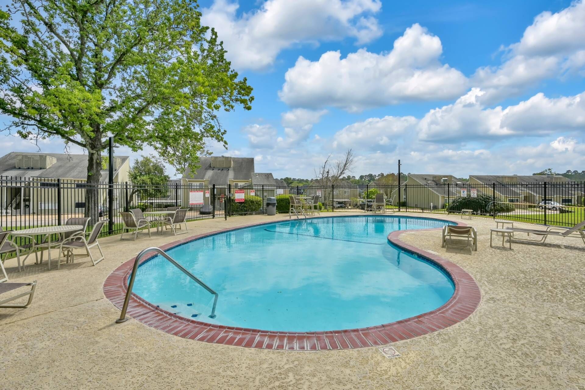 A swimming pool with a brick border, surrounded by a fence, and outdoor seating.