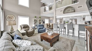 A spacious living area with a high ceiling, a dining area with a bar, and a kitchen with modern appliances. - Lake Conroe Waterfront | Pool + Swim/Fish Steps Away | King Suite | Patio + Amazing Views | Sleeps 6 (Montgomery)