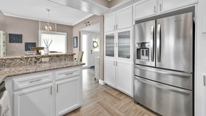 A modern kitchen with white cabinetry, a stainless steel refrigerator, and a marble countertop. - Lake Conroe Waterfront | Pool + Swim/Fish Steps Away | King Suite | Patio + Amazing Views | Sleeps 6 (Montgomery)