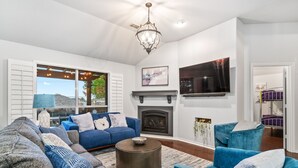 A modern living room with a blue sofa set, a fireplace, and a mounted TV. - Unique heated pool & spa outdoor kitchen, game room near DFW  sleeps 10-12 (Lewisville)