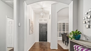 A hallway with a dark door, a white wall with a light fixture, and a dining area with a table and chairs. - Unique heated pool & spa outdoor kitchen, game room near DFW  sleeps 10-12 (Lewisville)