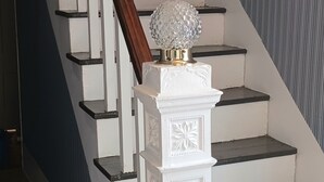 A staircase with white steps and a wooden handrail, leading to a landing with a decorative white balustrade and a crystal globe atop a pedestal.