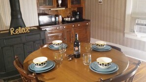A dining area with a round wooden table set for four, surrounded by wooden chairs. A black stove with a 'Relax' sign is visible to the left.