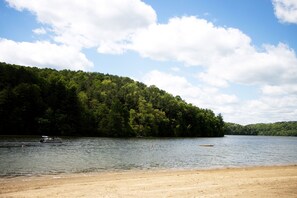 A beach with a forested hill in the background and a boat on the water.