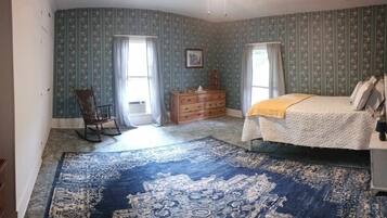 Ein Schlafzimmer mit Bett, Kommode, Schaukelstuhl und einem großen, gemusterten Teppich.