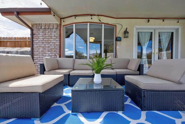 A covered patio area with wicker furniture, a glass coffee table, and a view of the landscape through glass doors. - Home with Heated Pool, Hot Tub and Amazing MT View (El Paso)
