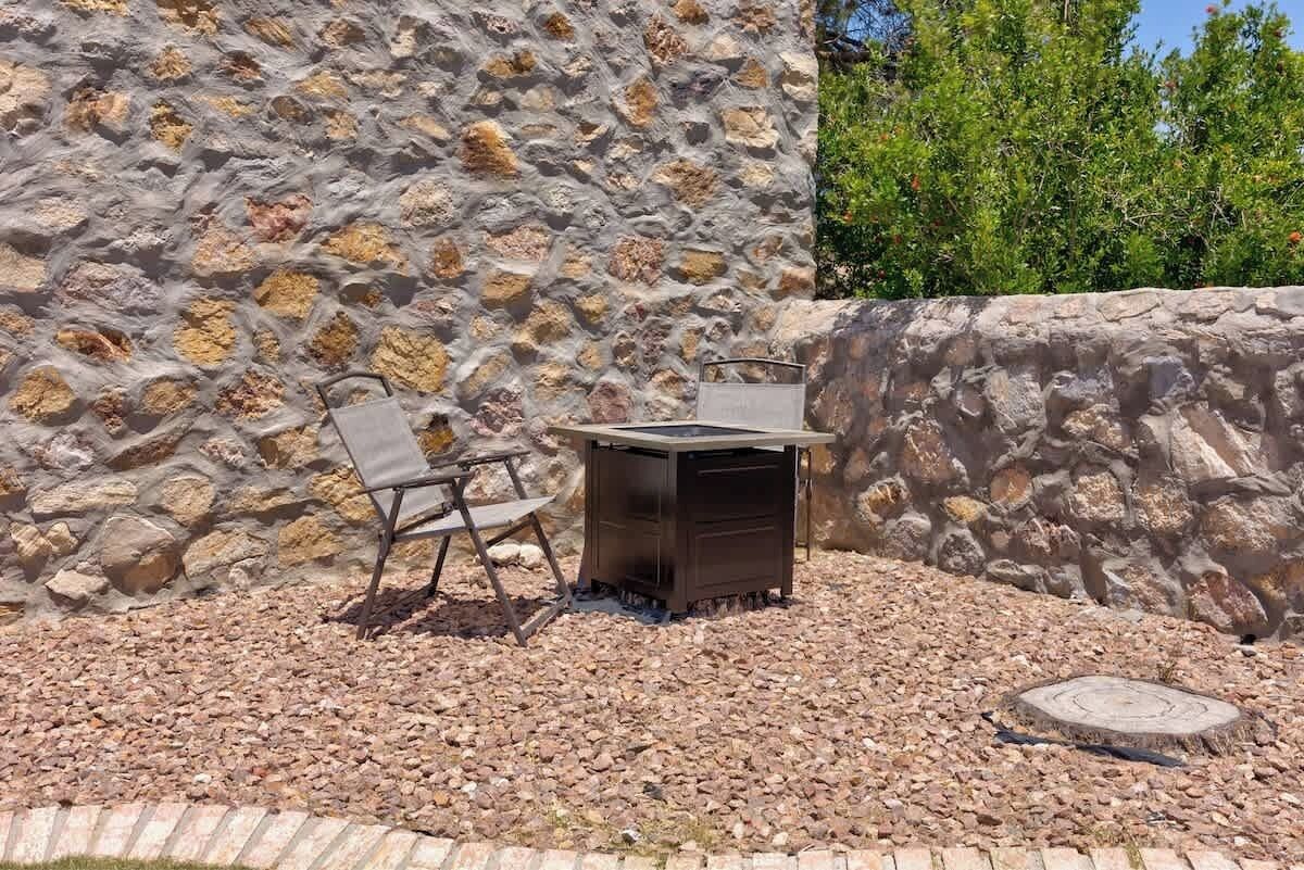 Un espace extérieur aménagé avec un mur en pierre en arrière-plan, un barbecue en métal et une chaise pliante.