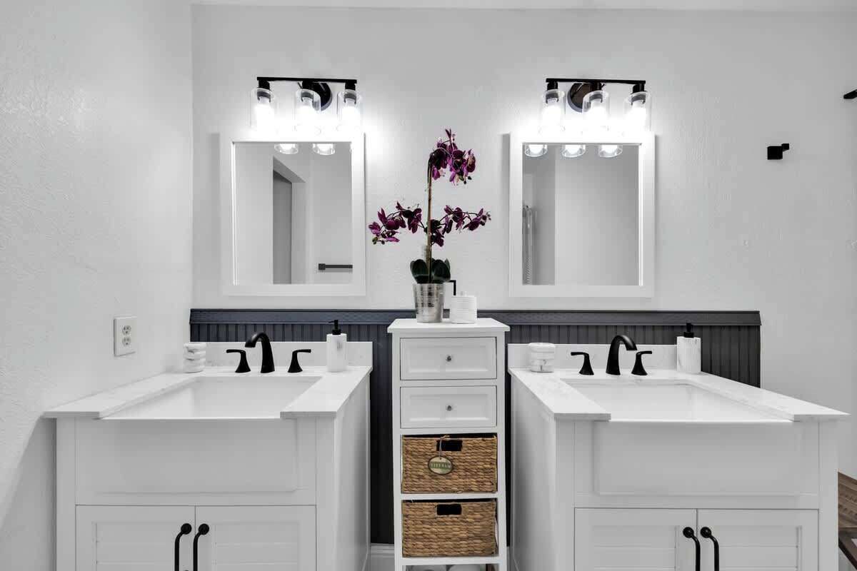 Une salle de bain avec deux lavabos, un miroir au-dessus de chaque lavabo et un vase central orné de fleurs.