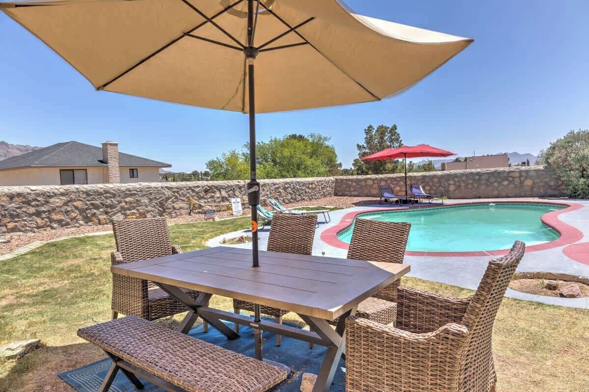 Un patio trasero con piscina, mobiliario exterior y un muro de piedra.
