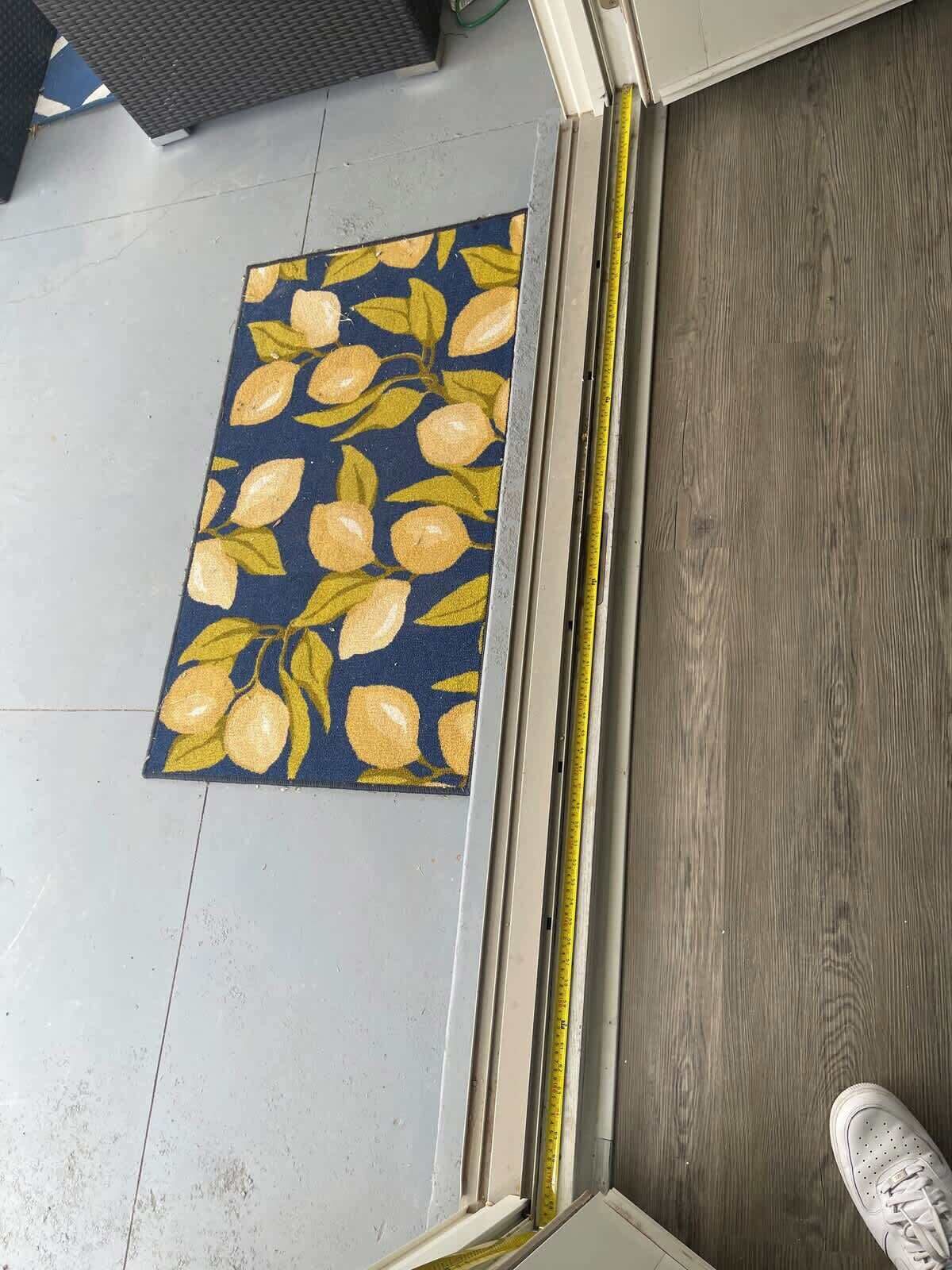 Esquina de una habitación con un tapete azul oscuro con limones y hojas amarillas, suelo de madera y un zapato blanco en el piso.