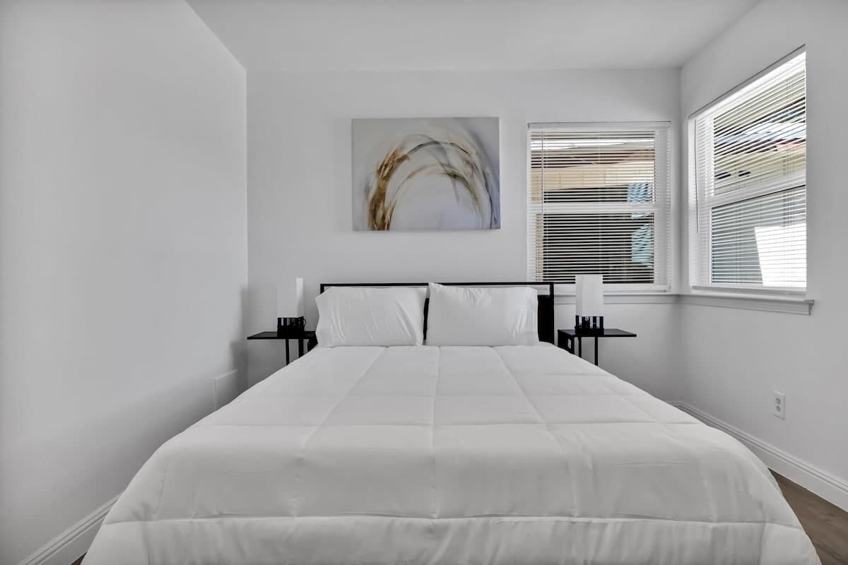 Un dormitorio con una cama grande, una mesita de noche, una silla y una ventana con persianas.