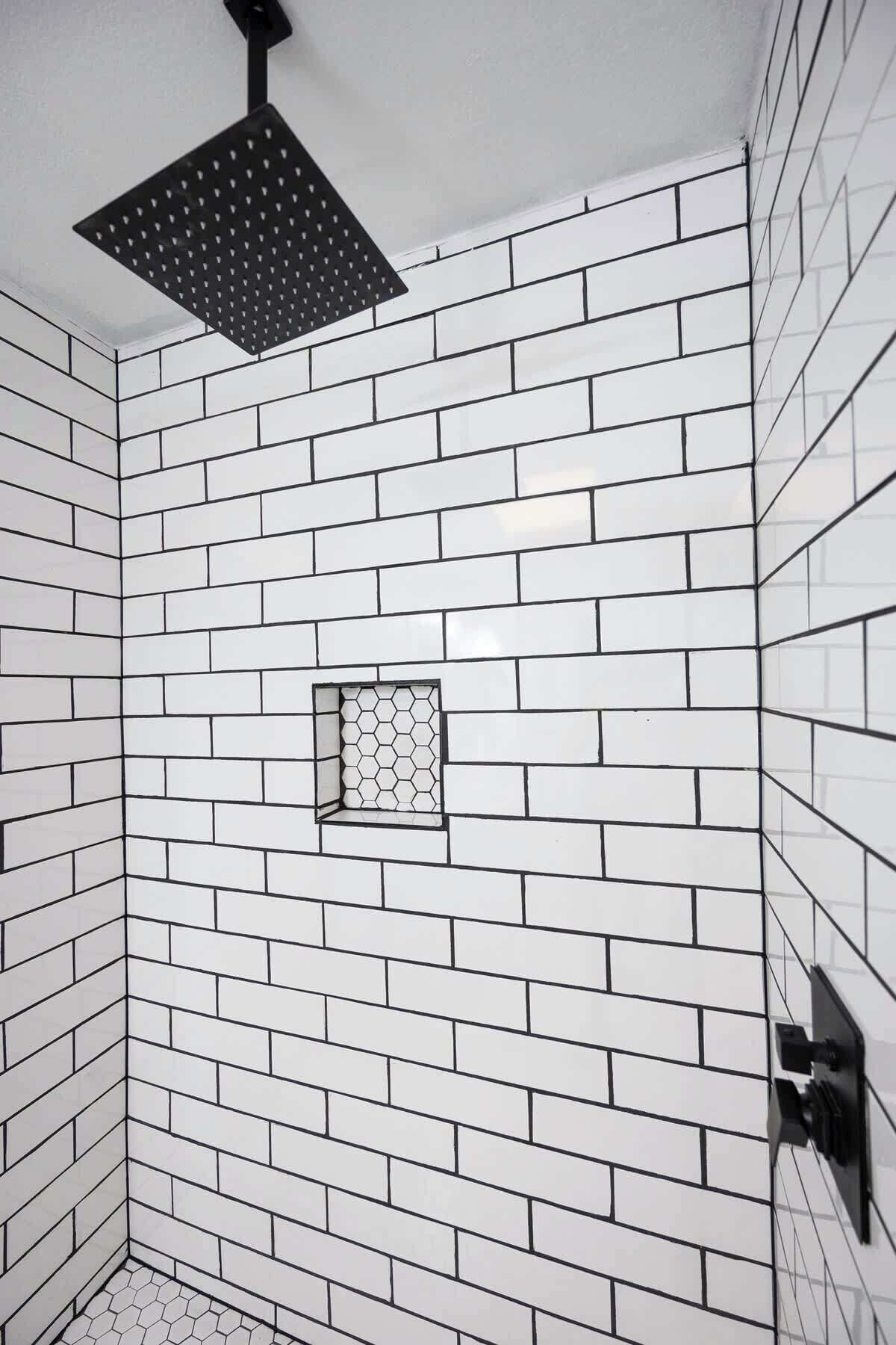 Douche met witte metrotegels en een zwarte douchekop.