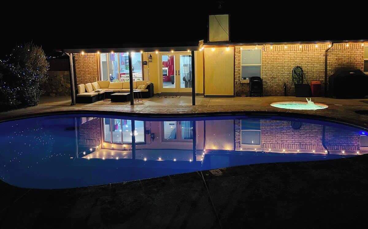 Un jardin avec une piscine, un espace salon couvert et un mur en briques.