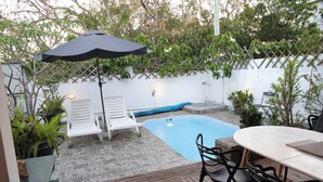 En trädgård med en pool, solstolar, ett bord och ett parasoll.