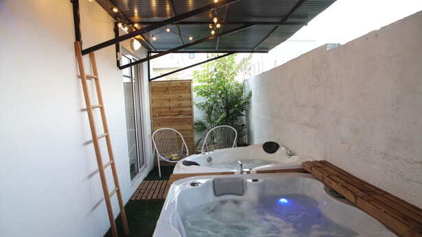 Ett spaområde med två bubbelpooler under ett tak, en trästege och en liten sittgrupp med stolar.