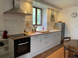 A modern kitchen with white cabinetry, a built-in oven, a stove, a window, and a clock on the wall.