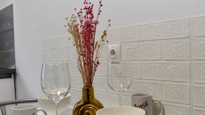 A dining table with a white bowl, two wine glasses, a gold vase with dried flowers, and two white mugs with text. - Toia Studio (Brasov)