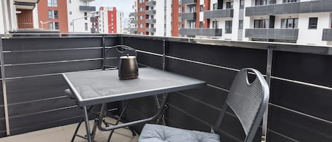 Un balcón con mesa y silla, un hervidor y vistas de edificios cercanos.