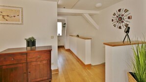 Un'ampia sala con pavimento in legno, un settimino in legno, una pianta in vaso e un elemento decorativo a parete.
