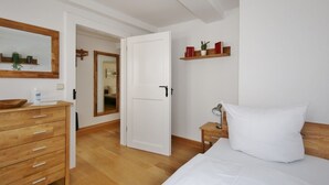 Una camera da letto con una cassettiera in legno, un letto con biancheria bianca, un comodino con una lampada e uno specchio appeso al muro.