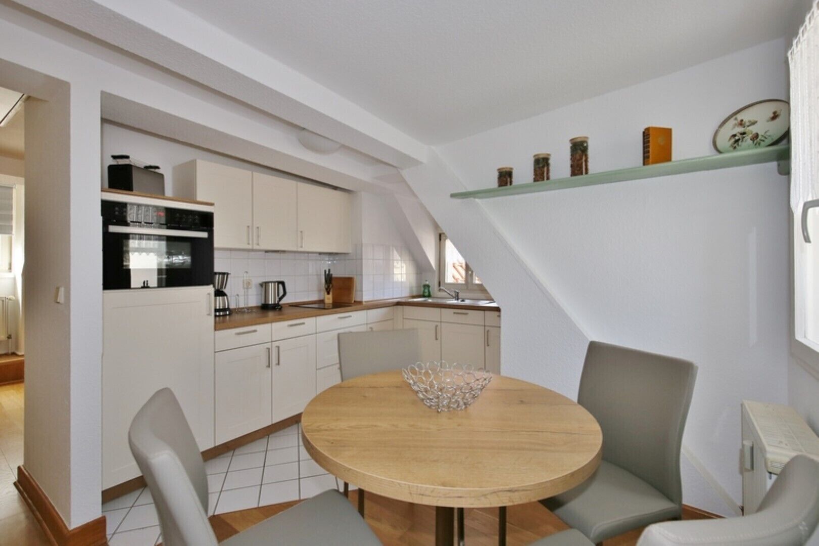 A modern kitchen with white cabinets, a wooden dining table, and a built-in oven.