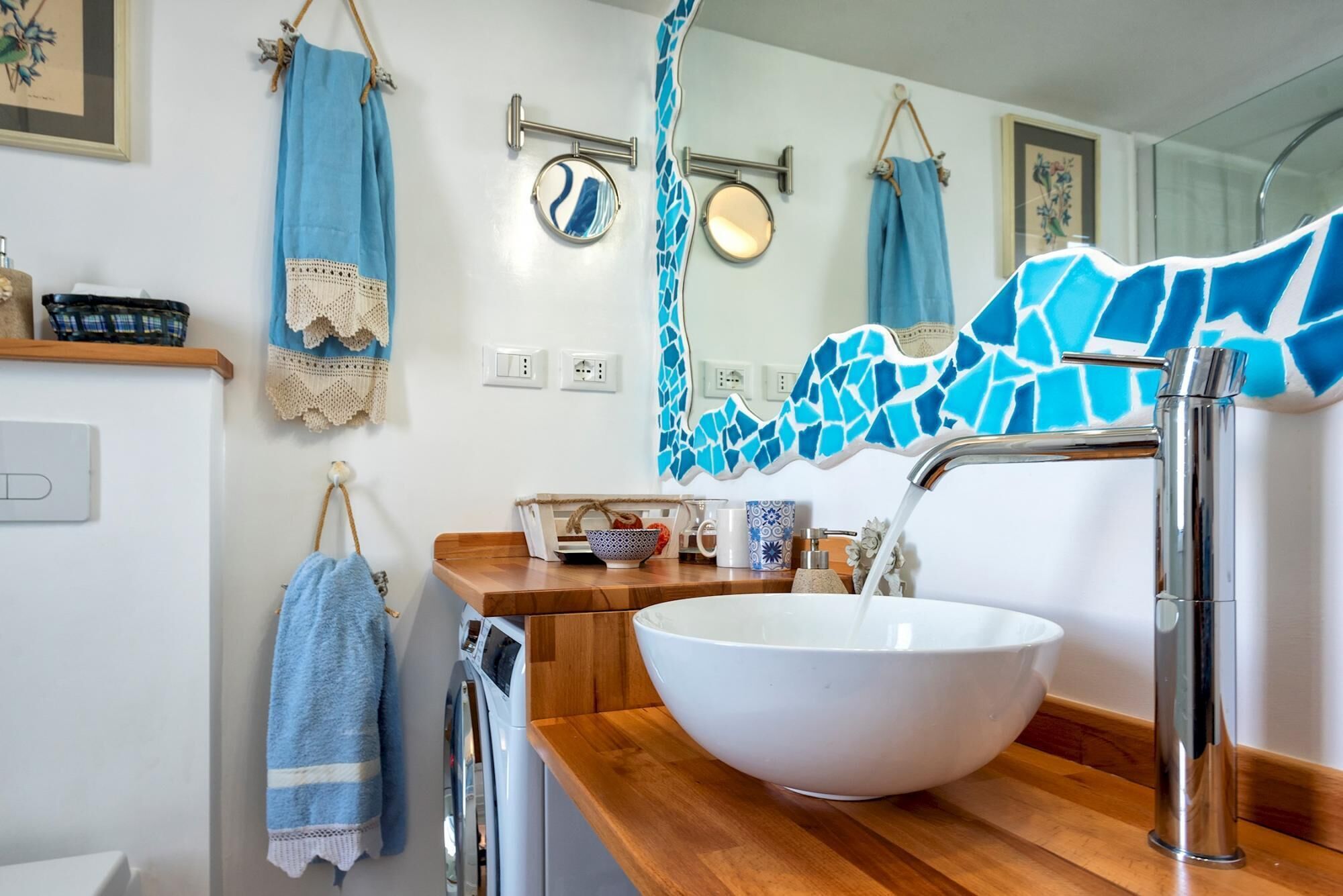 A bathroom with a white sink, blue towels, a washing machine, and a mirror with a blue mosaic backsplash.