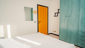 A bedroom with a bed, a wooden door, a wardrobe, and a mirror on the wall.
