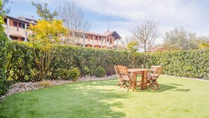 A well-maintained lawn with a wooden table and chairs, surrounded by a hedge and a building with multiple balconies in the background. - Il Giardino Dell Eden- Italian Homing (Sirmione)
