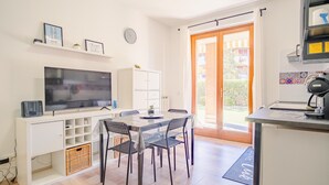 A modern kitchen with a large TV, dining table, and chairs. - Il Giardino Dell Eden- Italian Homing (Sirmione)