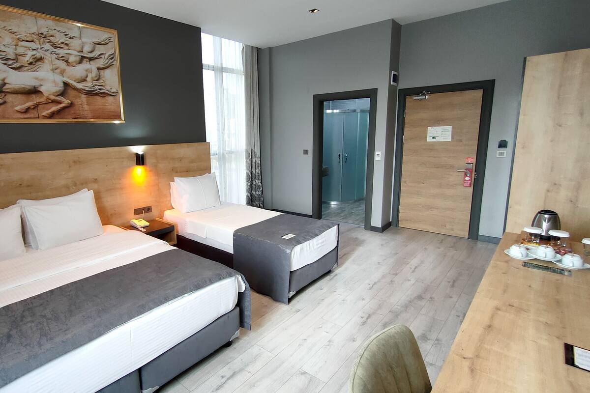 A hotel room with two beds, a desk with a coffee maker, and a painting on the wall.