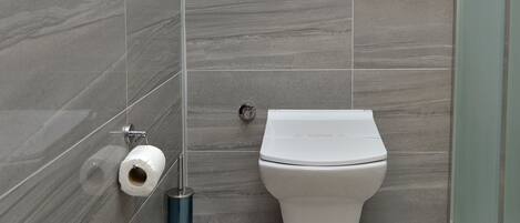 A modern bathroom with grey tiles, a toilet, a trash bin, and a towel rack.